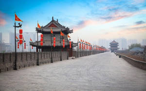 古老的石城牆上掛著紅燈籠和旗幟，在黎明天空下，背景是現代建築。 — 唐人街 GIF 壁紙