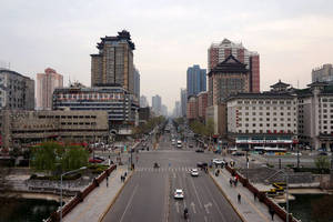 城市街道景觀，有傳統和現代建築、汽車和行人，天空多雲。 — 唐人街 GIF 壁紙