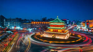 古老塔樓在黃昏時被照亮，周圍是城市迴旋處中旋轉的交通燈光。 — 神之塔 壁紙