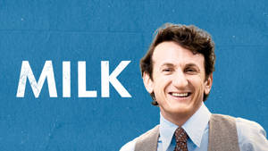 一個穿著背心同領帶嘅男人，喺藍色牆上MILK字樣旁邊微笑。