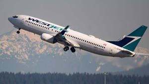 西捷航空飛機以山脈和森林為背景起飛。