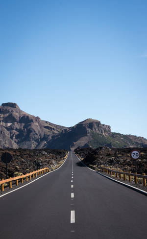 藍天下穿過火山地形的長直道路，遠處有山巒。