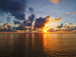 夕陽映照海洋，彩色雲朵和金色水面倒影