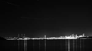 夜間城市天際線倒映在水中，天空有飛機尾跡 — 天際線 壁紙