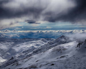 暴風雨天空下，陽光穿透雲層照耀的雪山山脈。