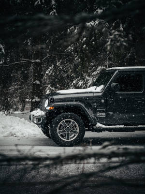 黑色Jeep Wrangler停泊在冬季森林雪路上，降雪中。