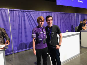 兩位男子在TwitchCon活動中，在紫色品牌布幕前擺姿勢。
