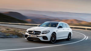 白色Mercedes-AMG E63 S Estate在日落時分行駛在蜿蜒的山路上。