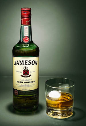 Jameson愛爾蘭威士忌酒瓶同杯，杯中有冰塊，放喺灰色表面上。