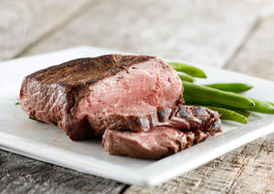 切片嘅 medium-rare 牛扒配青豆，放喺白色碟上，擺喺木質表面。