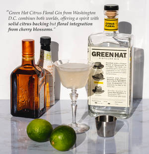 Green Hat氈酒瓶、雞尾酒杯和青檸放在大理石上，附有描述文字。