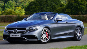 銀色 Mercedes-AMG 開篷車停泊在道路上，後面有綠色樹木。 — 汽車 壁紙
