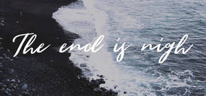 黑暗的火山海灘，海浪拍打，白色草書文字寫著「The end is nigh」。 — 語錄 壁紙