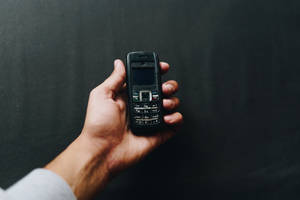 手拿著一部黑色復古手機，背景是深色的。 — Nokia 壁紙