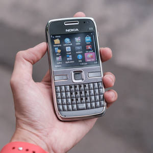 手拿著一部銀色Nokia E72手機，帶有實體鍵盤和活躍屏幕。 — iPhone 鎖定畫面 GIF 壁紙