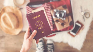 手拿護照放在打開行李箱上方，內有旅行物品 — 旅行 壁紙