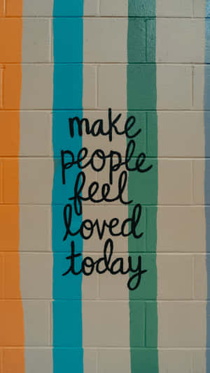一面彩色條紋牆，上面用黑色草書寫著 make people feel loved today 的訊息。