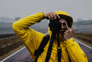 身穿黃色雨衣的人，在霧氣道路上手持相機並做出和平手勢。