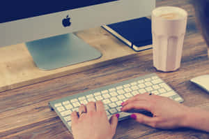 在 iMac 附近的木桌上，有人用鍵盤打字，旁邊有咖啡杯。 — 桌面美學 壁紙