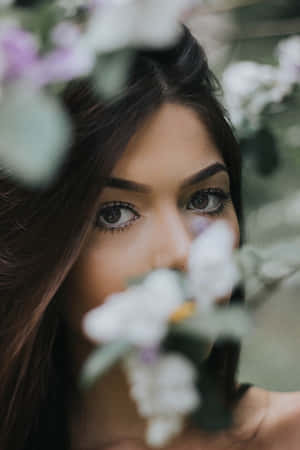 深色眼睛的女性在柔焦肖像中透過白色和紫色花朵窺視。