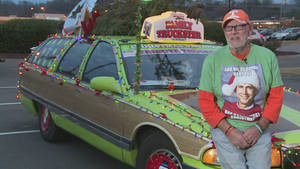 男子與一輛以 Family Truckster 為主題的聖誕裝飾旅行車合影。