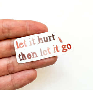 手拿著一個勵志貼紙，上面寫著「let it hurt then let it go」。 — 語錄 壁紙