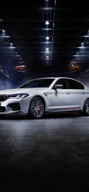 白色BMW M5跑車在光線昏暗的工業車庫中，配有聚光燈和煙霧。 — 銀河A 壁紙