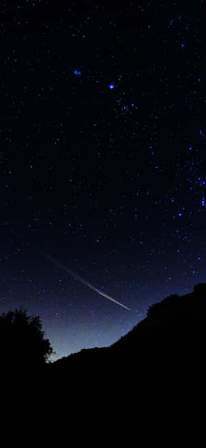 一顆流星在黑暗山丘和樹木上方劃過星空夜空留下一道軌跡。