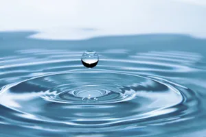 懸浮的水滴在平靜的藍色水面上產生漣漪。