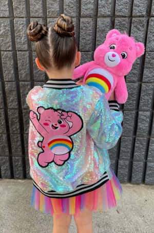 小孩穿著閃粉Care Bear外套和彩虹芭蕾舞裙，抱著毛絨熊。