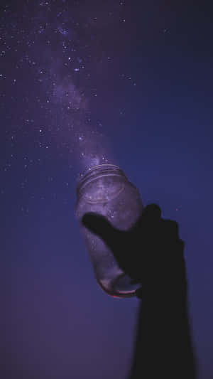 在紫色夜空下，一隻手拿著裝滿星星的罐子的剪影。