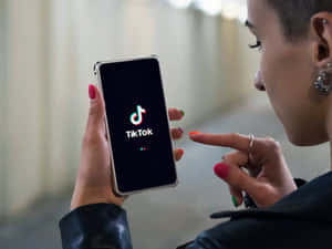 人拿著打開了TikTok應用程式的電話，並指向屏幕。 — TikTok GIF 壁紙