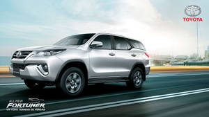 銀色豐田 Fortuner SUV 在碼頭附近的海岸道路上快速行駛。