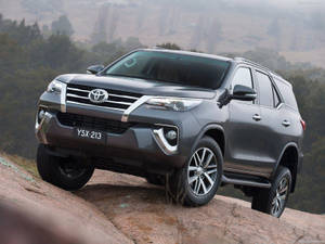 灰色豐田 Fortuner SUV 在森林背景下攀爬岩石山坡 — 汽車 壁紙