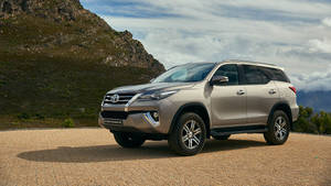 銀色豐田 Fortuner SUV 停泊在岩石地形和多雲天空的山路上。