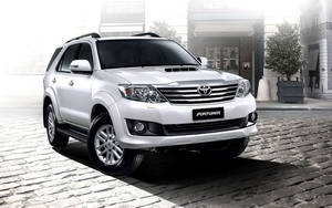 白色豐田 Fortuner SUV 停泊在建築物附近的鵝卵石街道上