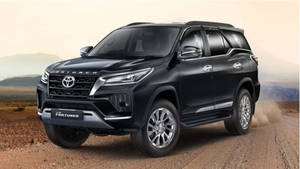 黑色豐田 Fortuner SUV 在沙漠的泥路上行駛，背景有山脈。 — 汽車 壁紙