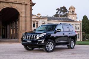 黑色豐田Land Cruiser SUV停在帶有拱門和鐘樓的歷史石建築前。