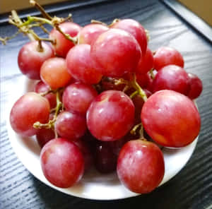 一碗飽滿的紅葡萄放在深色木質表面上。