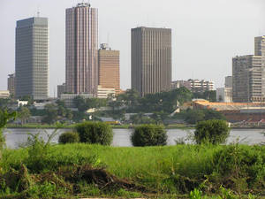 城市天際線，高樓大廈位於河流和前景的綠草之後。 — 橙色城市 壁紙