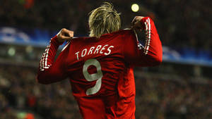 足球運動員 Torres 在夜間將紅色 9 號球衣拉過頭頂慶祝。