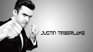 Justin Timberlake 身穿黑色西裝，在灰色漸變背景前舉起拳頭。 — 拳擊 壁紙