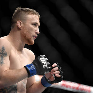 一位有紋身的男性MMA拳手戴著UFC手套站在八角籠內。