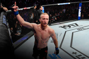 一位赤裸上身的MMA選手在UFC八角籠內高舉雙手慶祝勝利。