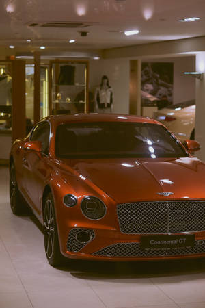 一輛亮橙色的賓利 Continental GT 展示在豪華車展廳中。