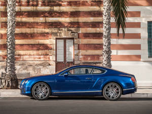 藍色 Bentley 跑車停泊在街上，旁邊有棕櫚樹和舊建築。