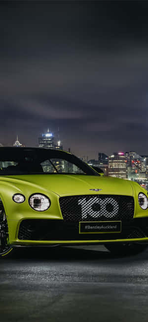 青檸綠色賓利跑車夜間停放，背景是城市燈光。 — iPhone Air 壁紙