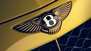 深色格柵的豪華汽車引擎蓋上的金色 Bentley 翅膀標誌。 — 金色美學 GIF 壁紙