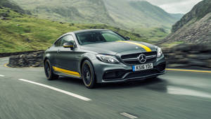 灰色Mercedes-AMG C63 Coupe帶黃色條紋在山路上行駛。