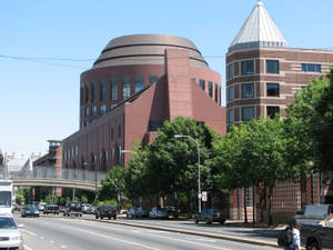 城市街景，現代磚砌建築與綠樹在清澈藍天下相映成趣。